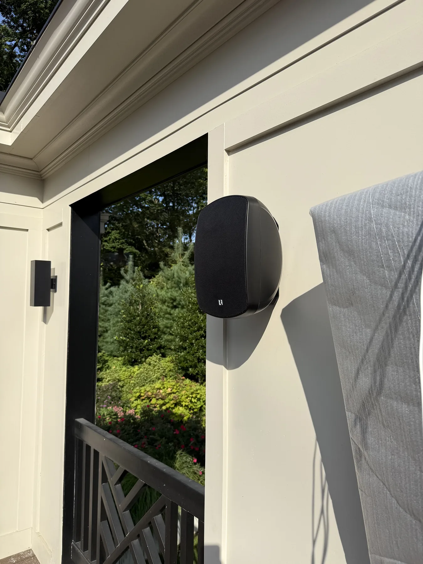 Black outdoor speaker mounted on a white patio pillar