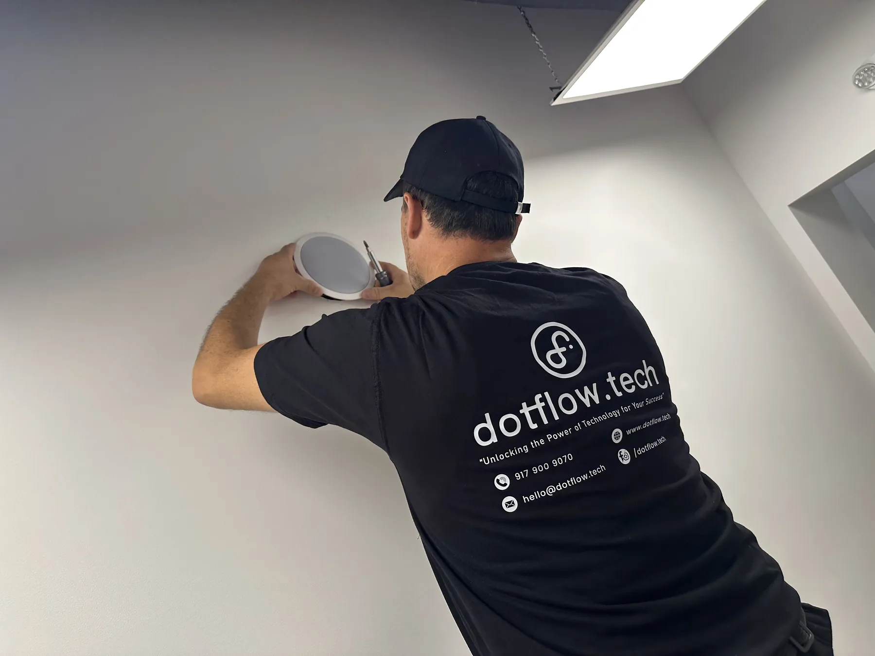 Technician installing a white in-ceiling speaker overhead