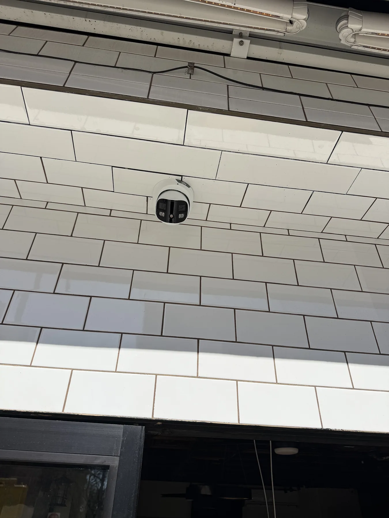 Small circular security camera on a white tiled wall