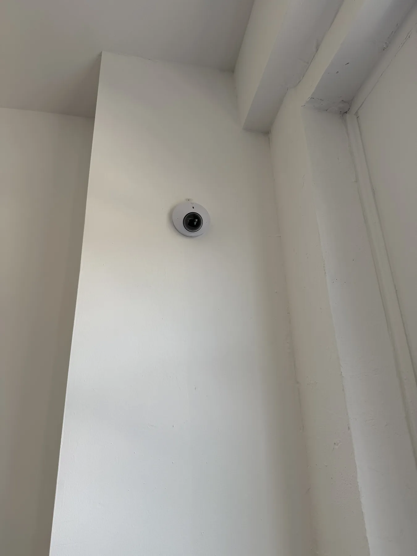 Small circular security camera at a wall-ceiling corner