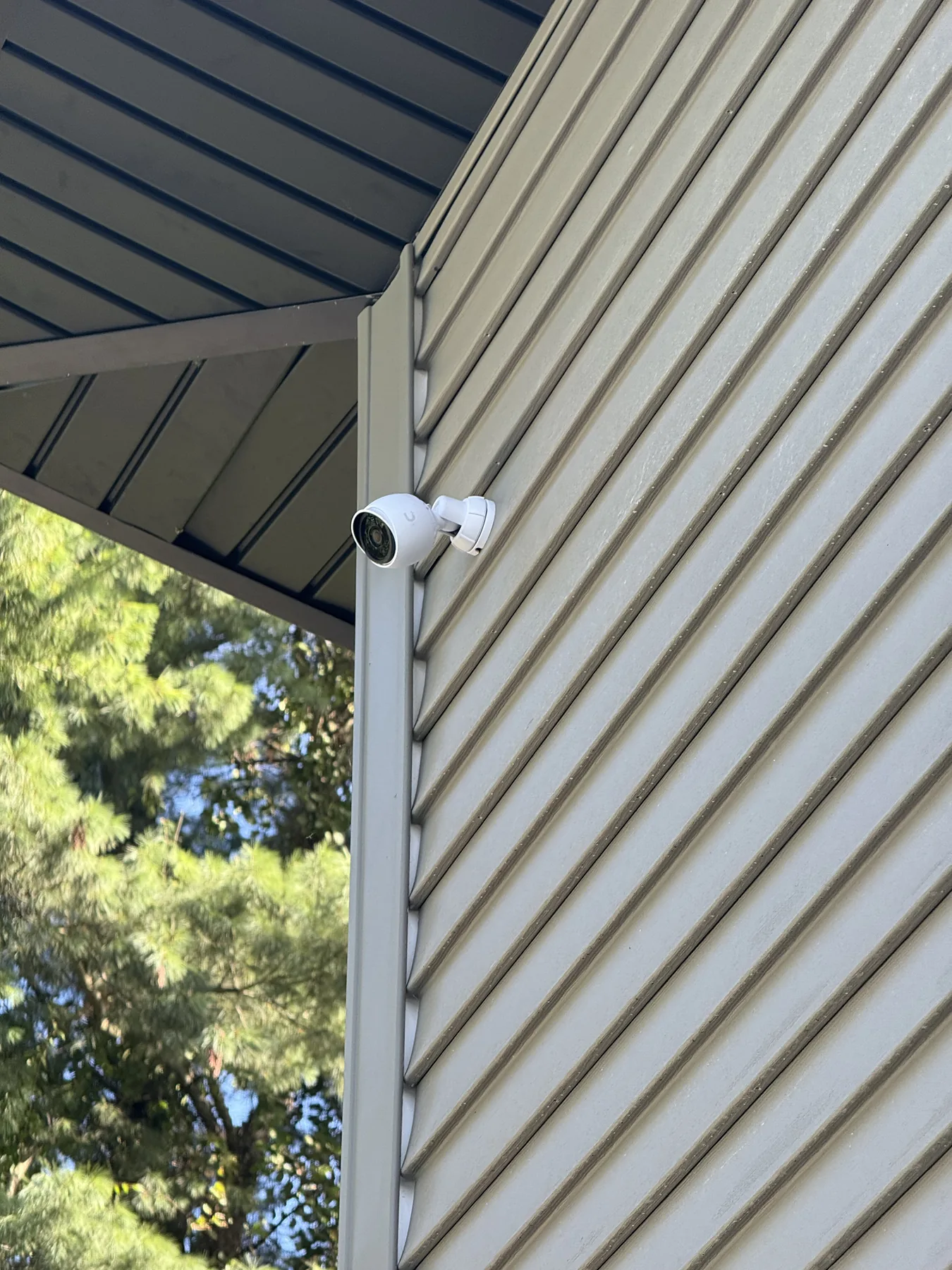 White bullet security camera on house siding overlooking woods