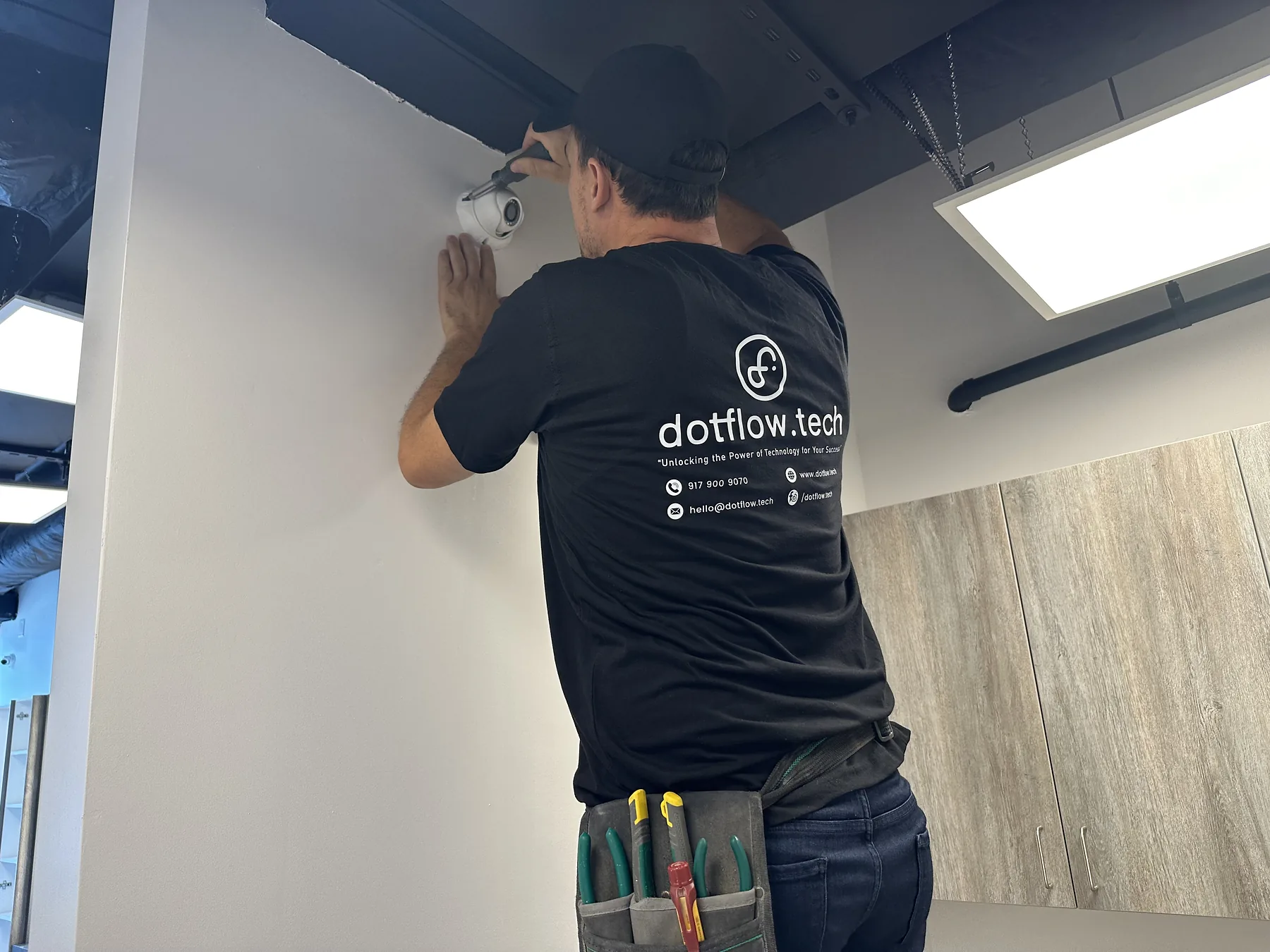 Technician installing a white dome security camera high on a wall