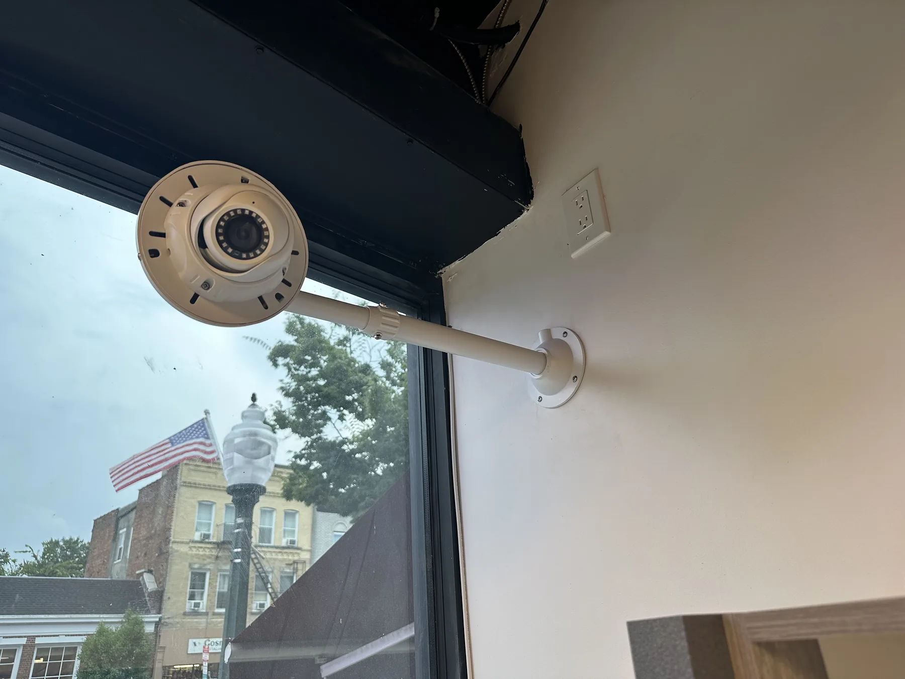 Tan dome security camera on a pendant arm near a window